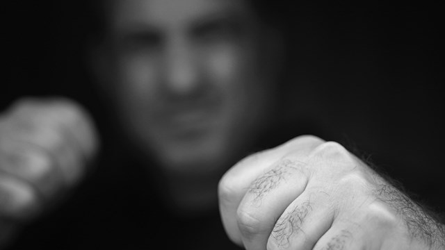 Portrait of abusive aggressive man punching fists from the darkness.