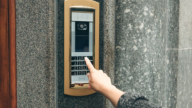 A female hand presses the buttons on the intercom for access inside.