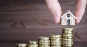 Placing a miniature houses on top of a coins stack against a wooden background. Building a step by step mortgage plan