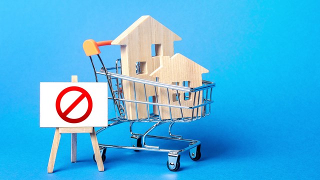Houses in a shopping cart and easel red prohibition sign NO. Inaccessibility, lack housing, deficit. Seizure, freezing of assets by a bank, court. Expensive maintenance, impossibility of restoration