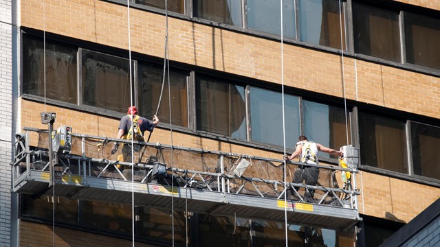 New York, New York, USA - August 5, 2010: Two men washing windows on a skyscraper. Working platform is raised and lowered by ropes.