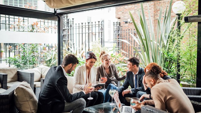 Group of business people are discussing their work in a bar courtyard after work. They are drinking cocktails and using technology.