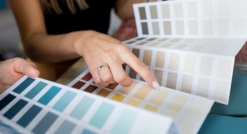 Close-up of two women choosing samples of wall paint. Interior designer consulting a client looking at a color swatch. House renovation concept