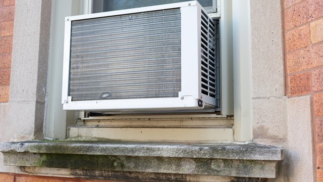 A simple window air conditioning unit seen from the outside on a brick urban residential building