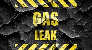 'GAS LEAK' warning sign in yellow block lettering on cracked black background 