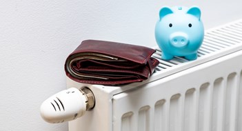 A stuffed wallet lying on the radiator and a small blue piggy bank, The concept of rising apartment heating costs