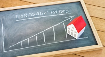 Graph representing the rise in mortgage interest rates drawn on a chalkboard lying on a wooden table. A model of a house with a red roof is on the chalkboard. Finance and real estate concept.