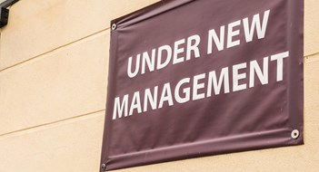 Changing Property Managers under new management sign banner on wall ouside shop in england.