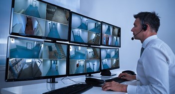 Rear view of security system operator looking at CCTV footage at desk in office