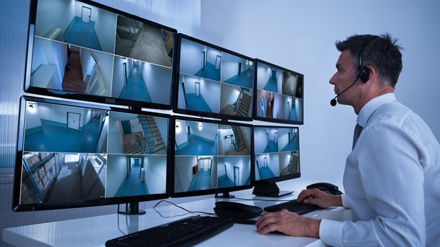 Rear view of security system operator looking at CCTV footage at desk in office