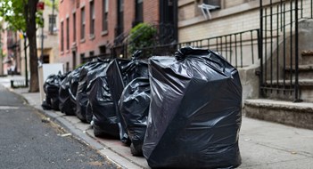 A row of black garbage bags along a residential street and sidewalk waiting to be picked up in Greenwich Village of New York City