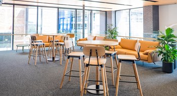 Meeting area in a modern creative coworking space with couch, sofa, bar stools, leaner tables, carpet. No people, modern building interior. 