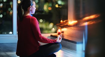 Girl doing yoga training at home at night. Young Latin American woman meditating using an app on smartphone.