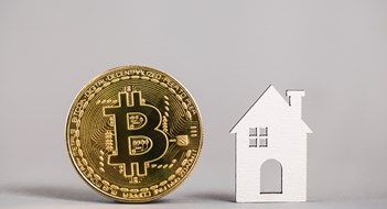 Kiev, Ukraine - May 18, 2021: Buying Property with Cryptocurrency. Buying real estate with bitcoin. Gold bitcoin coin, model house on gray background. property. Copy space.