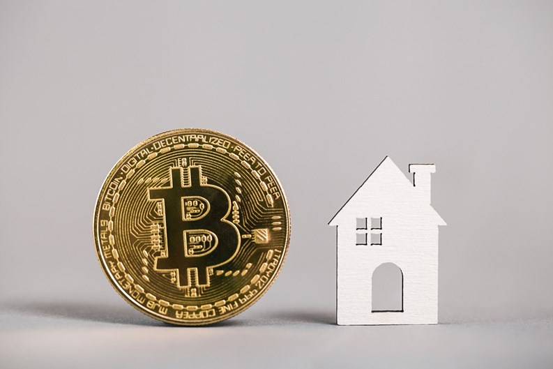 Kiev, Ukraine - May 18, 2021: Buying Property with Cryptocurrency. Buying real estate with bitcoin. Gold bitcoin coin, model house on gray background. property. Copy space.