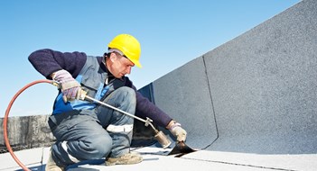 Roofer installing Roofing felt with heating and melting roll of bitumen roll by torch on flame