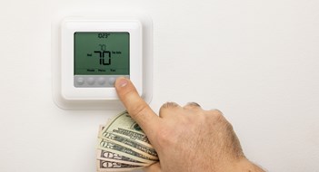 Energy Recovery Ventilators A hand holding money adjusting a thermostat on a wall.