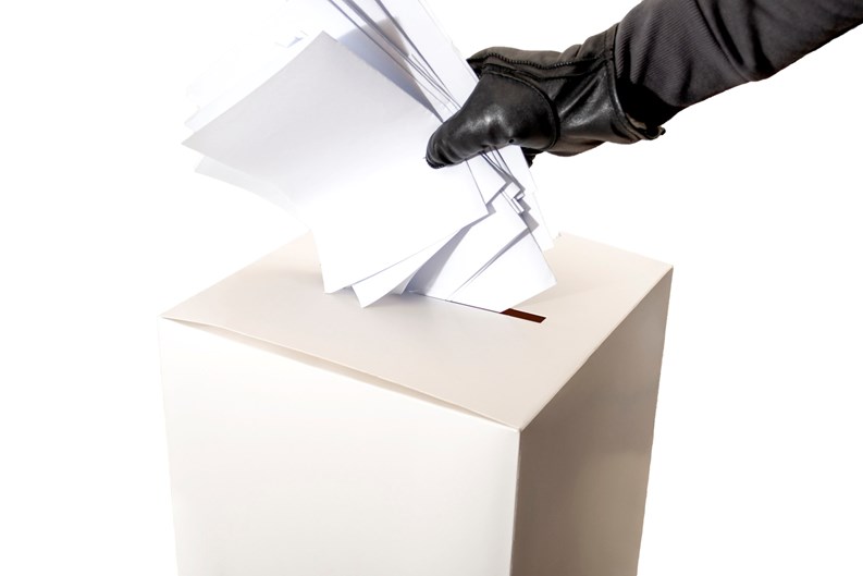 Electoral fraud and hacked elections concept with a hand wearing a leather glove and stuffing a ballot box isolated on white background with copy space and a clipping path cut out