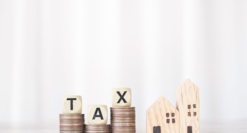 Study: NYCers Pay Median $6,317 in Property Taxes Annually Miniature house, Wooden blocks with the word TAX on stack of coins. The concept of payment tax for house, Property investment, House mortgage, Real estate.
