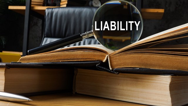 Legal liability concept. Law book and magnifying glass.