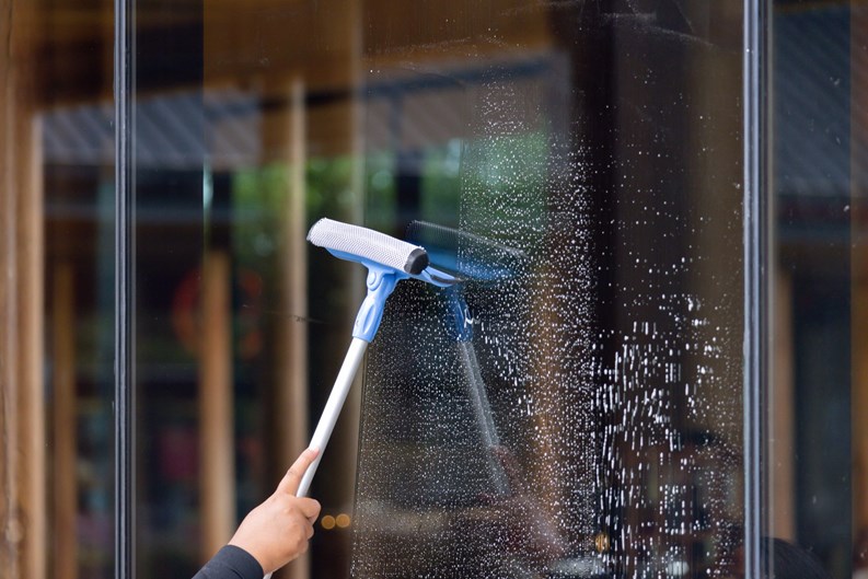 A person is cleaning a window with a squeegee. The window is covered in streaks and the person is using a blue and white squeegee to clean it