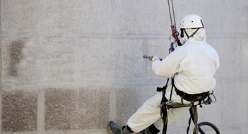 Façade Cleaning Belgrade, Serbia - April 21, 2018: Rope access facase maintenance; A worker wearing a protective gear cleaning a stone church exterior with abrasive blasting equipment