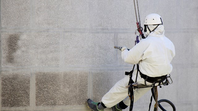 Belgrade, Serbia - April 21, 2018: Rope access facase maintenance; A worker wearing a protective gear cleaning a stone church exterior with abrasive blasting equipment