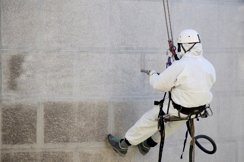 Belgrade, Serbia - April 21, 2018: Rope access facase maintenance; A worker wearing a protective gear cleaning a stone church exterior with abrasive blasting equipment