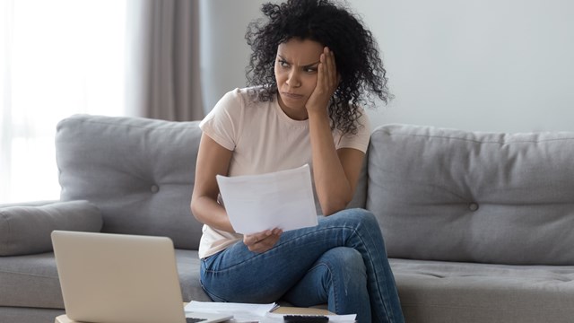 African woman sit on couch near pc received utility bills feels concerned about price increase or high taxes, female holds letter from bank about money debt overspend or credit loan rejection concept