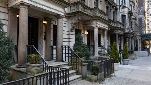 A row of old brick and stone residential building entrances along a sidewalk on the Upper East Side of New York City