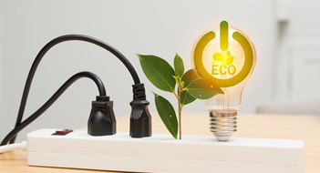 10 Steps to Reduce Energy Waste Small green plant and two black power cords plugged into a white power strip on a wooden desk, representing renewable energy, eco-friendly lifestyle, sustainability, environmental conservation concept