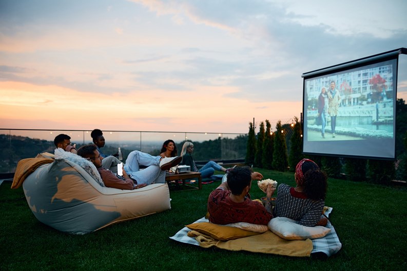 Multiracial friends enjoying in movie night in the backyard at sunset. Copy space.